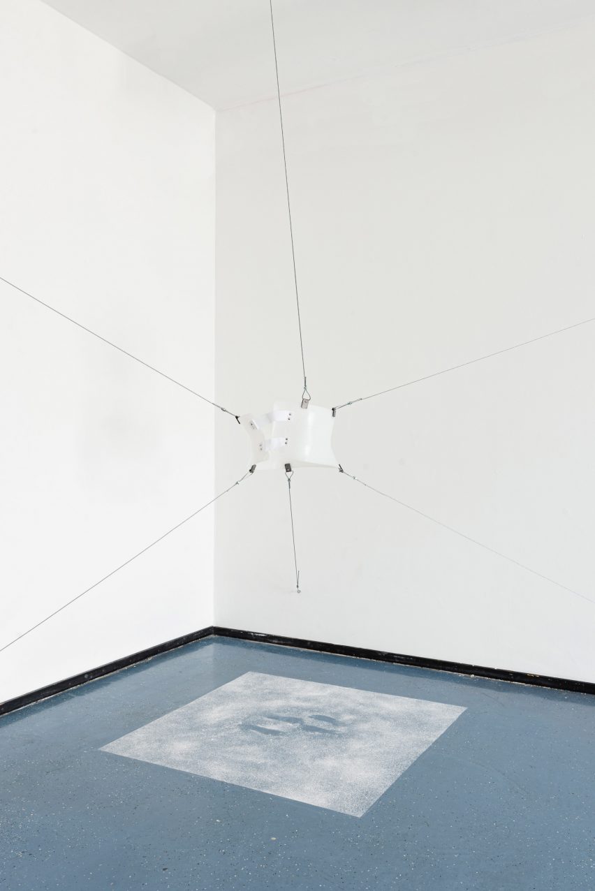 A photograph of a hanging white installation, in a room with white walls and a blue floor.