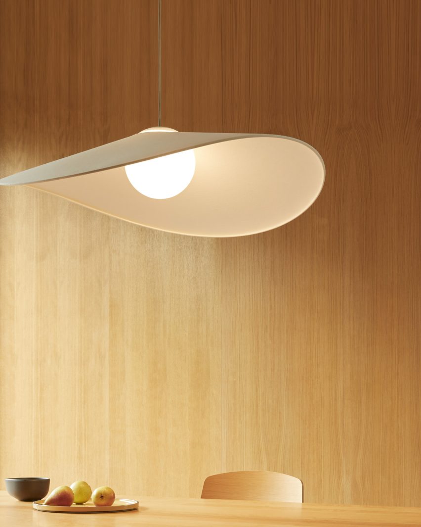 A photograph of a pendant light in white tones against a beige wooden wall