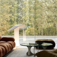 A photograph of a floor lamp in tones of white, in a living room placed in front of a glass window