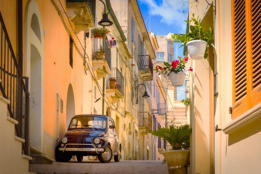 A photograph of a street in an Italian town, with a small brown car parked on it