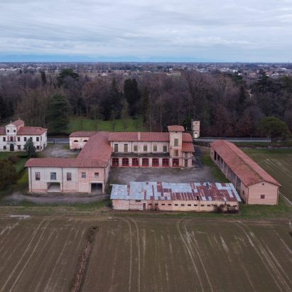 A photograph from above of a large stone building within a green field in tones of red and beige.