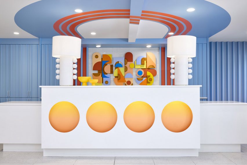 A hotel reception desk in front of a relief mural and a sky-blue backdrop