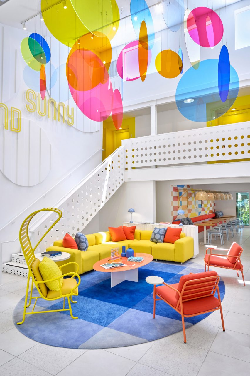 Citrus-hued furniture sits below a mobile of colourful circles in a double-height hotel lobby
