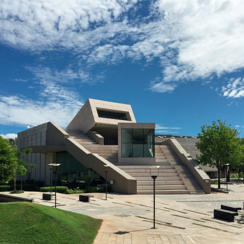 a photograph of a university campus in tones of grey, with a blue sky behind it