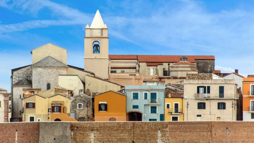 a photograph of stone buildings in colours of beige, blue and orange, against a blue sky.
