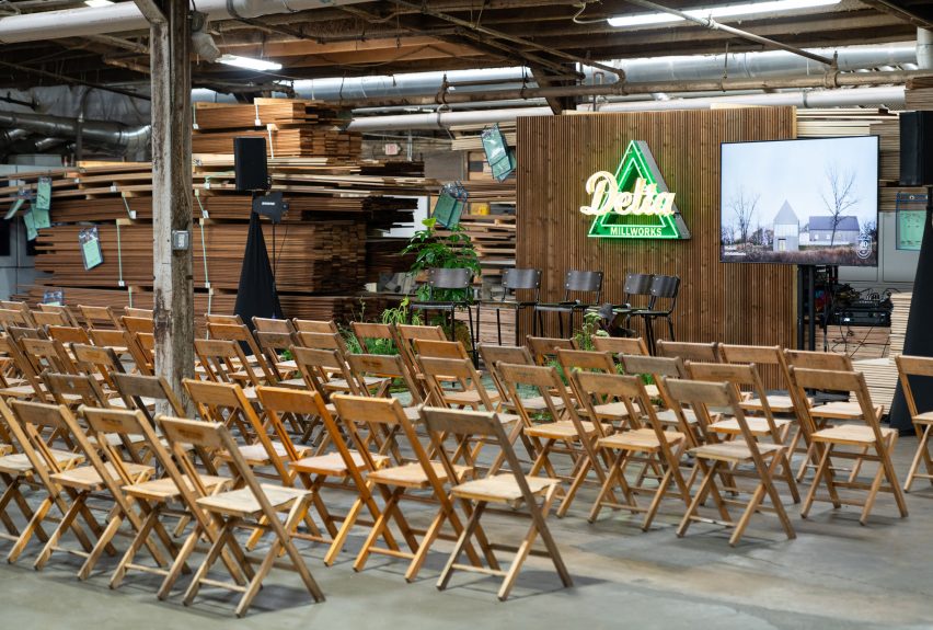 Photo of wooden folding chairs lined up in front of a small stage where a triangular neon sign reads Delta Millworks