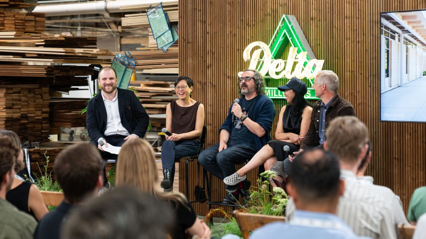 Photo of panel discussion speakers sitting on stools on stage with lumber behind them
