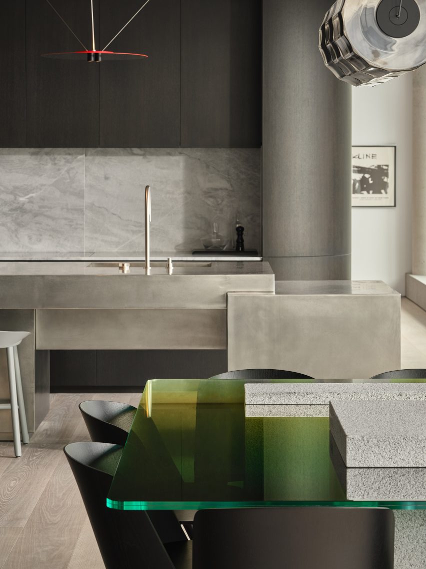 Green glass dining table in front of a metal kitchen