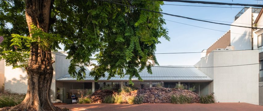 Gabled building behind mound of rocks and big tree
