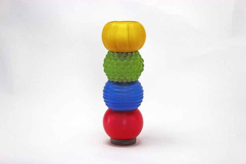 a photograph of a modular lighting system, displaying four lamps on top of each other in a vertical arrangement, in tones of red, blue, green and yellow against a grey backdrop