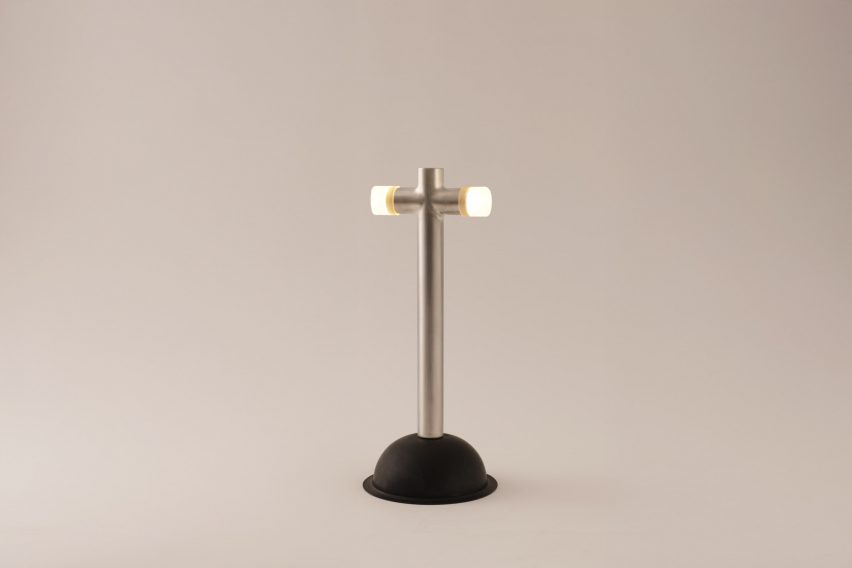 a photograph of a lamp built from a plunger, in tones of silver and black against a grey backdrop