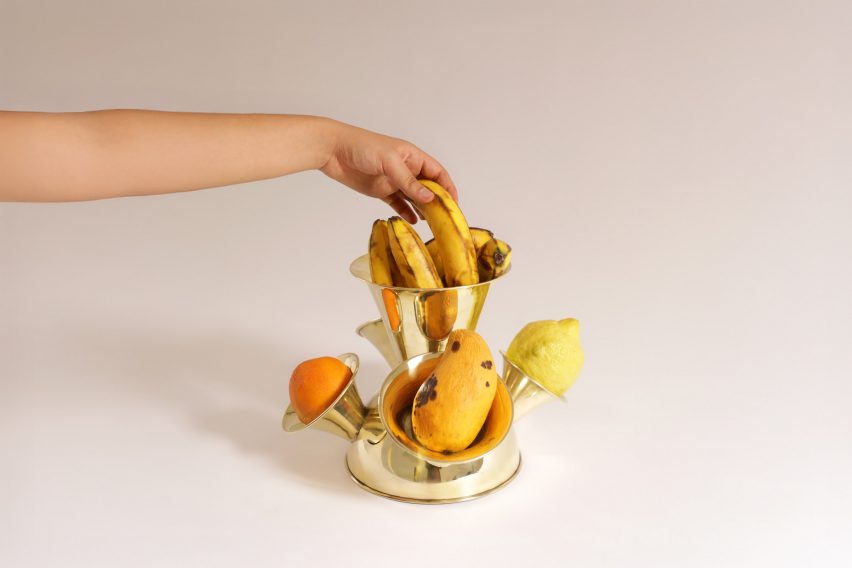 a photograph of a silver vessel which holding fruit. There is a person's hand taking a piece of fruit from it