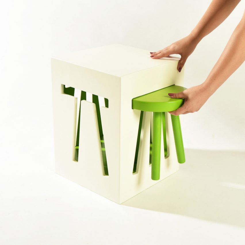 a photograph of a person interacting with an abstract stool design, featuring a white cube with a pull-out green stool in it.