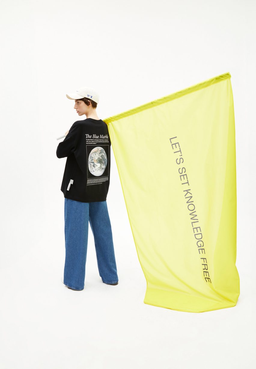 Person wearing long-sleeve shirt from Wikimedia Foundation and Armedangels collaboration holding a yellow flag that reads "Let's set knowledge free"