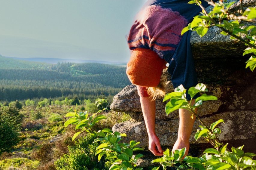 a photograph of a person hanging over a rock in a green landscape