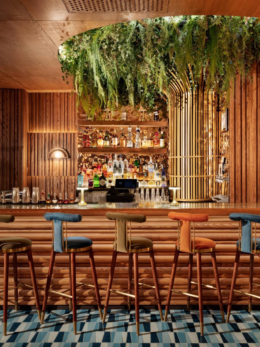 Bar with tall velour-upholstered stools and greenery hanging from the ceiling