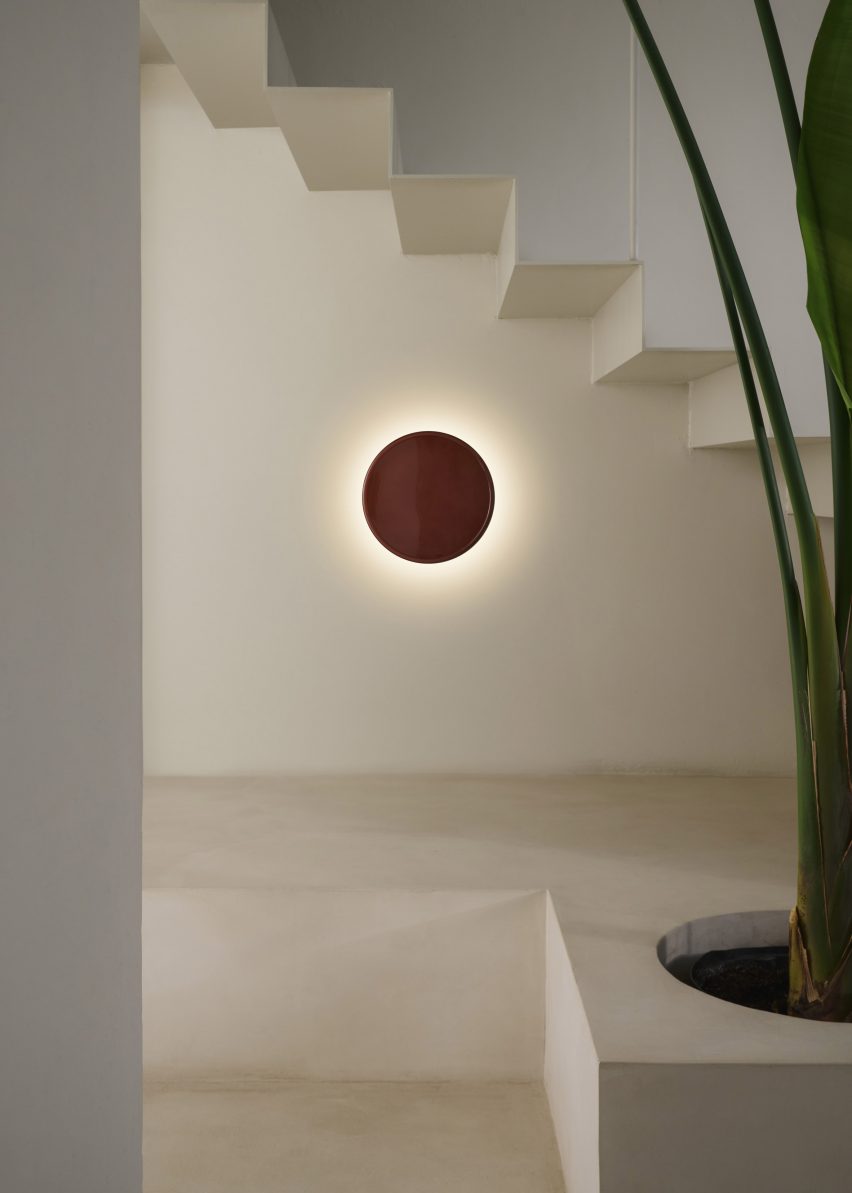 a photograph of a circular red wall light underneath a staircase