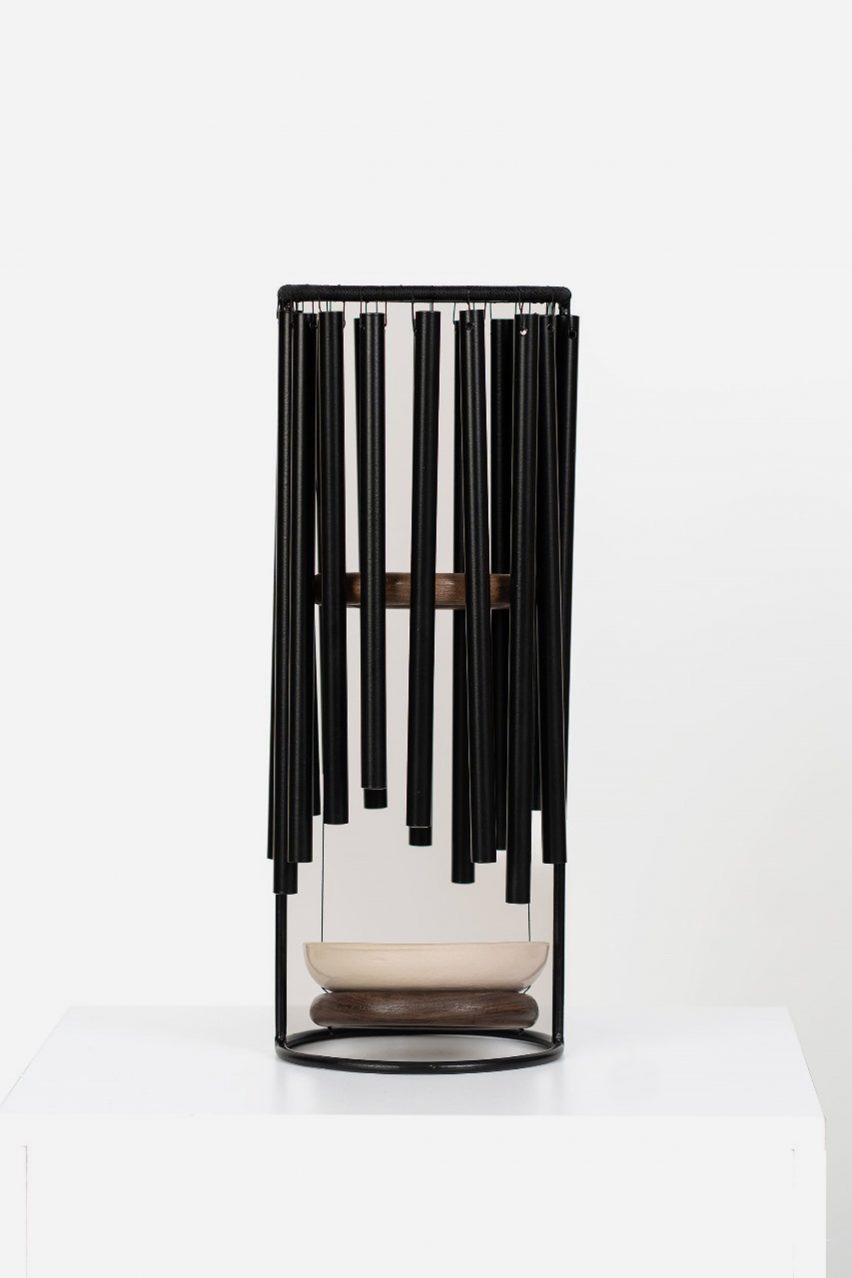 a photograph of an object which holds wind chimes with plates below them, in tones of black, beige and brown
