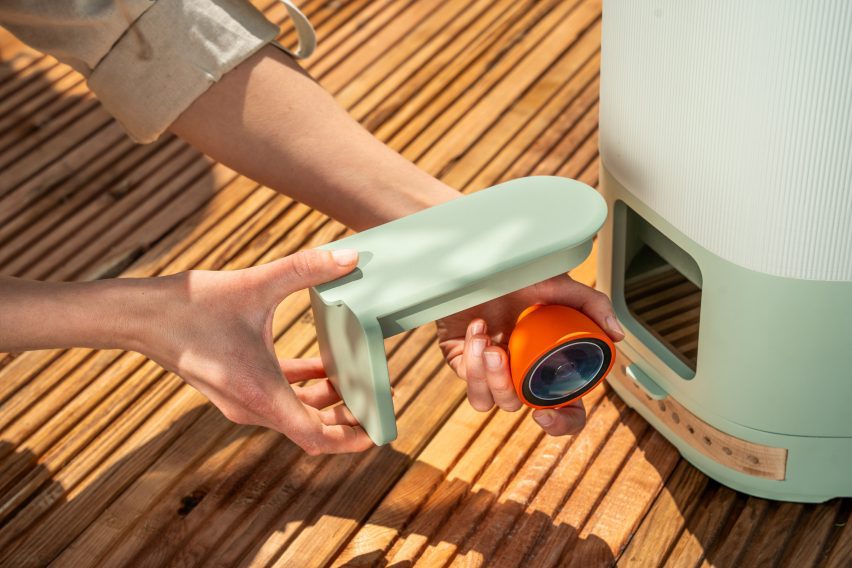 Photo of a person's hands removing a small, brightly coloured Petal camera for inside of a slot within a plastic garden bee habitat