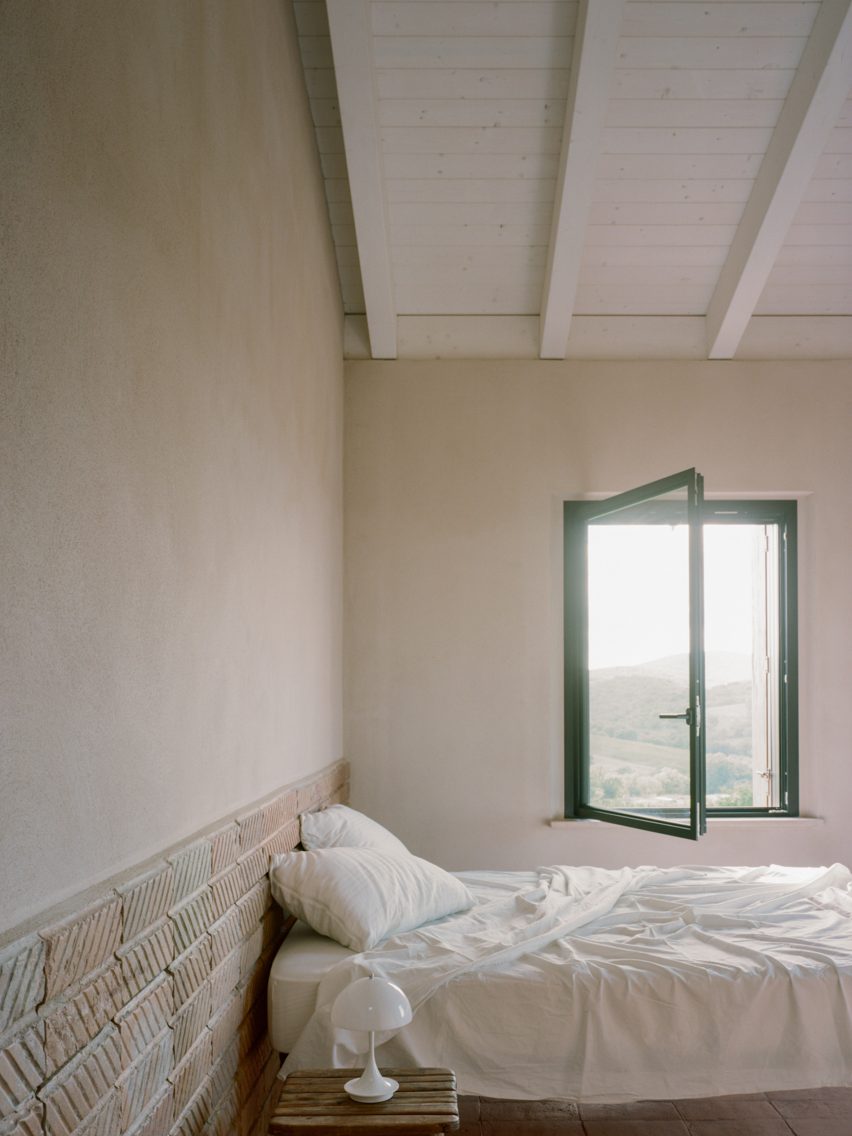 Unmade bed in high-ceilinged room with view of countryside through window
