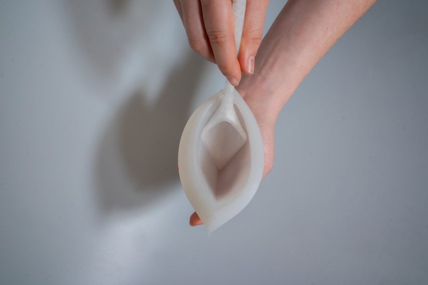 Photo of a person's hands holding a narrow silicon vessel with an angular, deep-bowled spoon resting in it