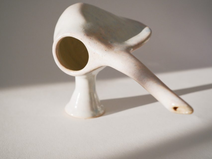 Photo of a strange-shaped ceramic vessel with one foot, a hole on one size, a narrow angular wall opposite that and a long spout