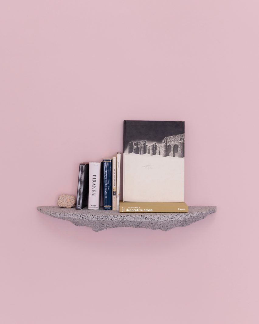 Photograph of the granite-looking, grey shelf holding books against a light pink backdrop.