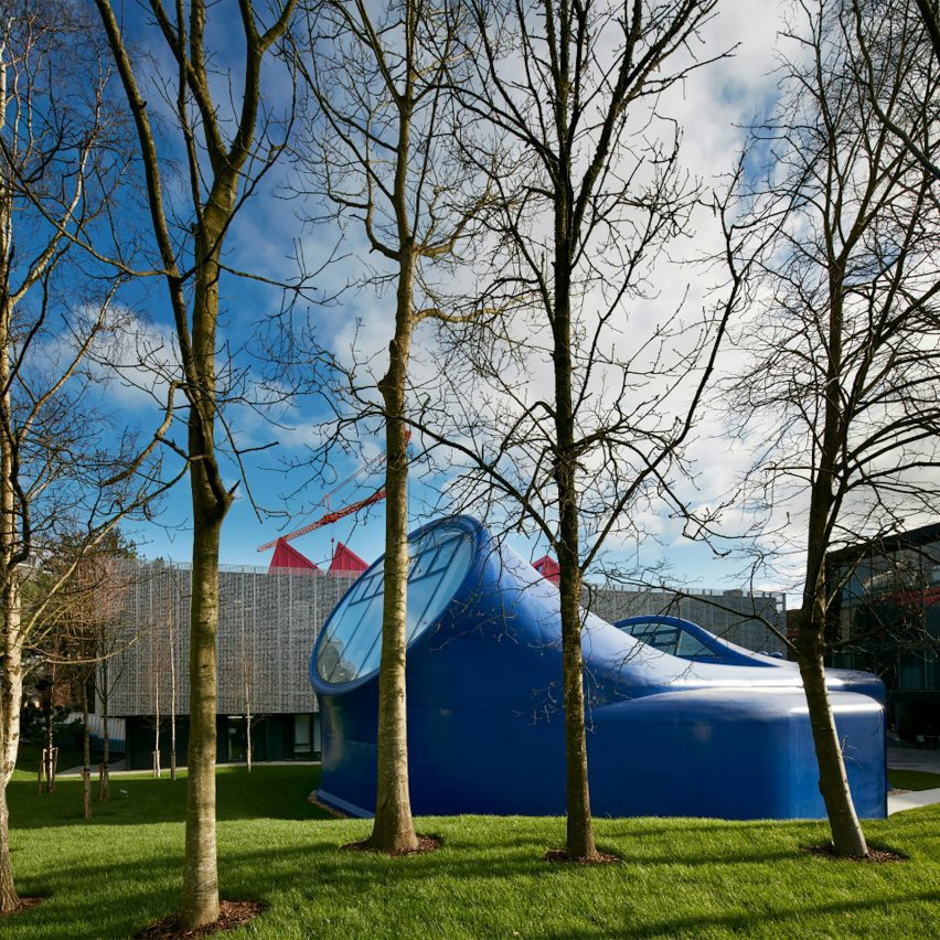 a photograph of a blue building among a green space