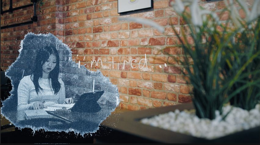 a photograph of an animation still displaying a person sat at a table against a brick wall