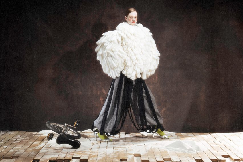a photograph of a model wearing a large white garment and black trousers