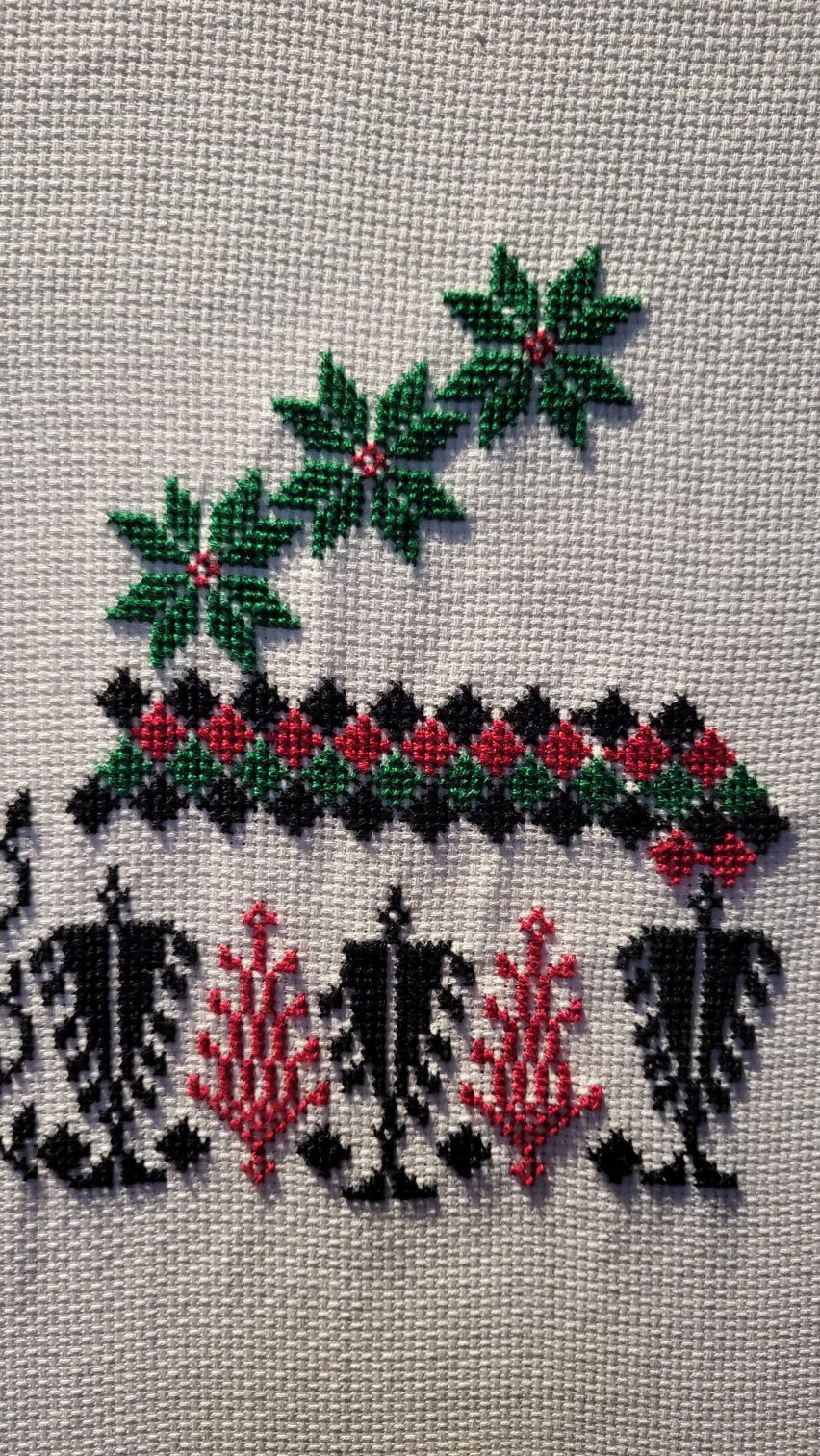 a photograph of a cross stitch in tones of black, green and red