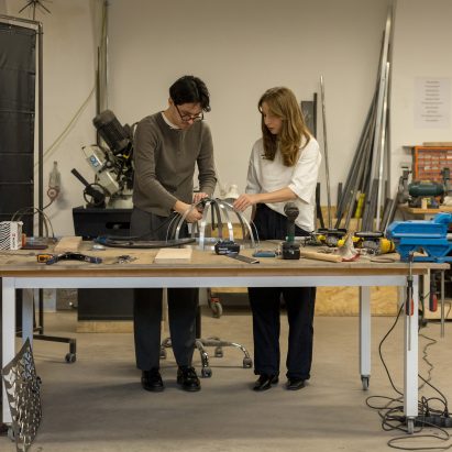 Two people in a workshop working on a metal structure