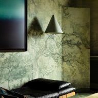 Photograph showing a green nature-inspired wallpaper, and a hanging pendant lamp over a wooden bench with a black leather covering.