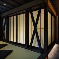 An image displaying large, washi-paper doors with dark wooden borders. There is a corridor going down the right side of the image and a small table with two futon-pillows on the floor for sitting.