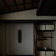 A photo containing a display shelf with in-built storage cabinets on the right side, and a beige wall on the left with a central light-fixture. There is a slanted ceiling with dark wooden beams at the top of the photo.