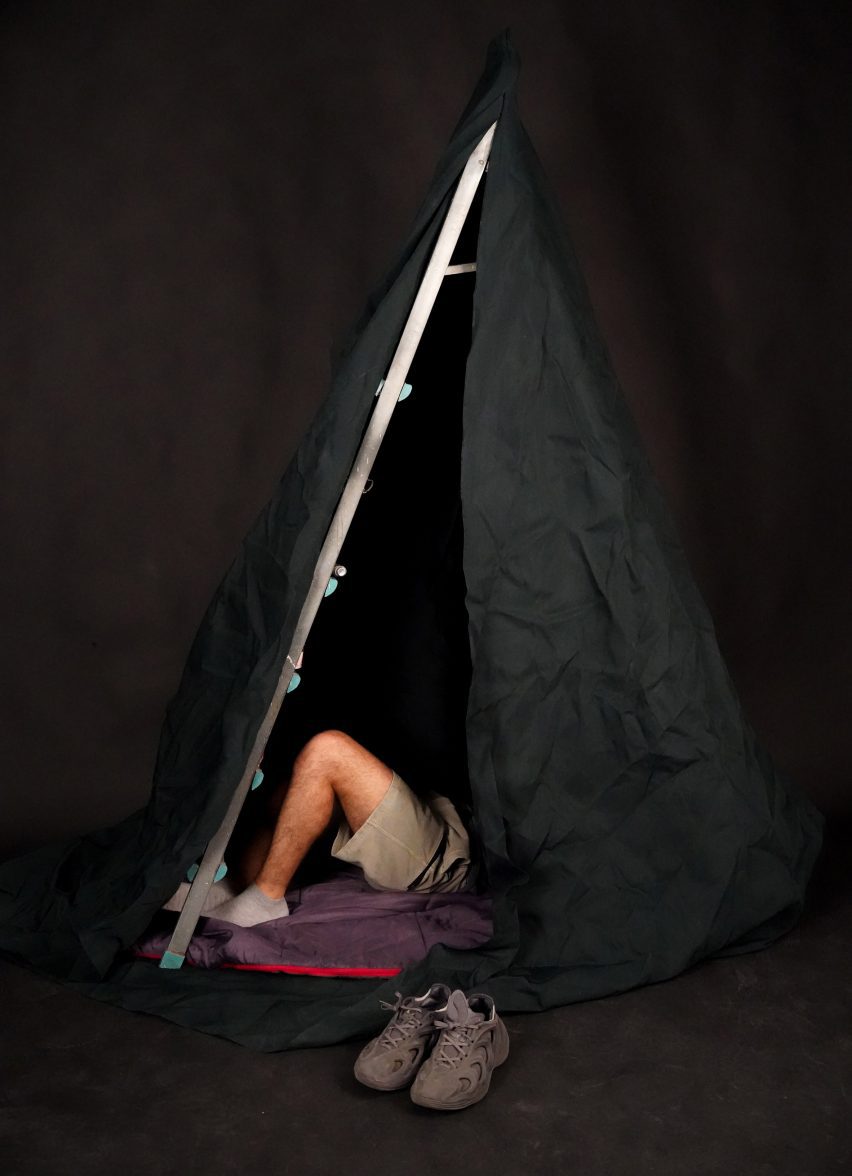 Photo of a tent structure fashioned from a ladder and a sheet with a person's legs sticking out from inside