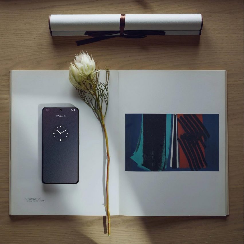 A flatlay image of the Punkt MC03 phone sitting on top of an open book on a desk alongside an elegant white flower