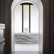 A free-standing marble bath can be seen through a single archway.