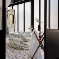 Image of a freestanding marble bathtub surrounded by frosted windows. Light pink, patterned tiles are on the floor.