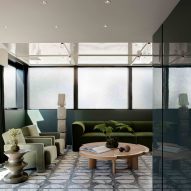 The top floor entertainment room shows patterned grey tiles, a wooden coffee table and a set of velvet green furnishings. Glass windows wrap around the room, and small stone sculptures stand between the sofas and armchairs.