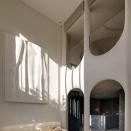 Image of a contemporary, white living room with a 3D printed artwork inspired by ocean waves, and stacked inverted arches that span two floors.