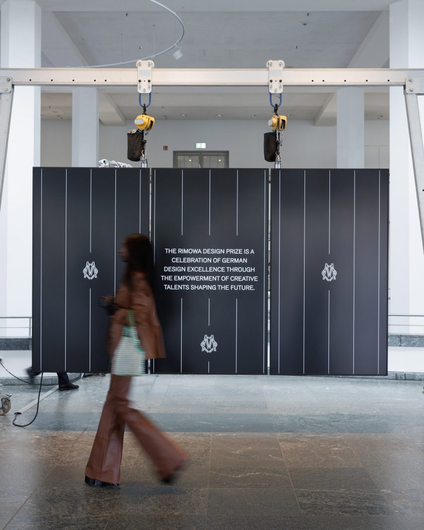 Visitor walking past the Rimowa Design Prize exhibition installation in a large gallery space