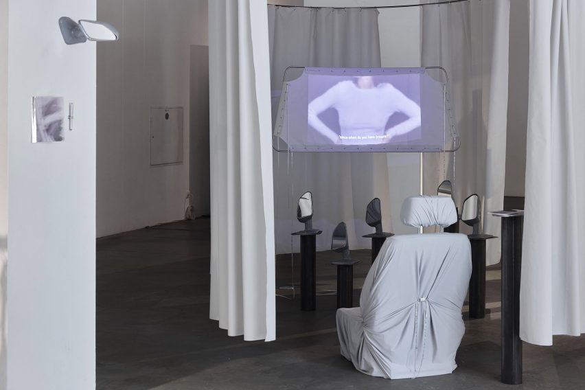Photograph of an installation with a large, white chair facing a number of mirrors and a projector screen.