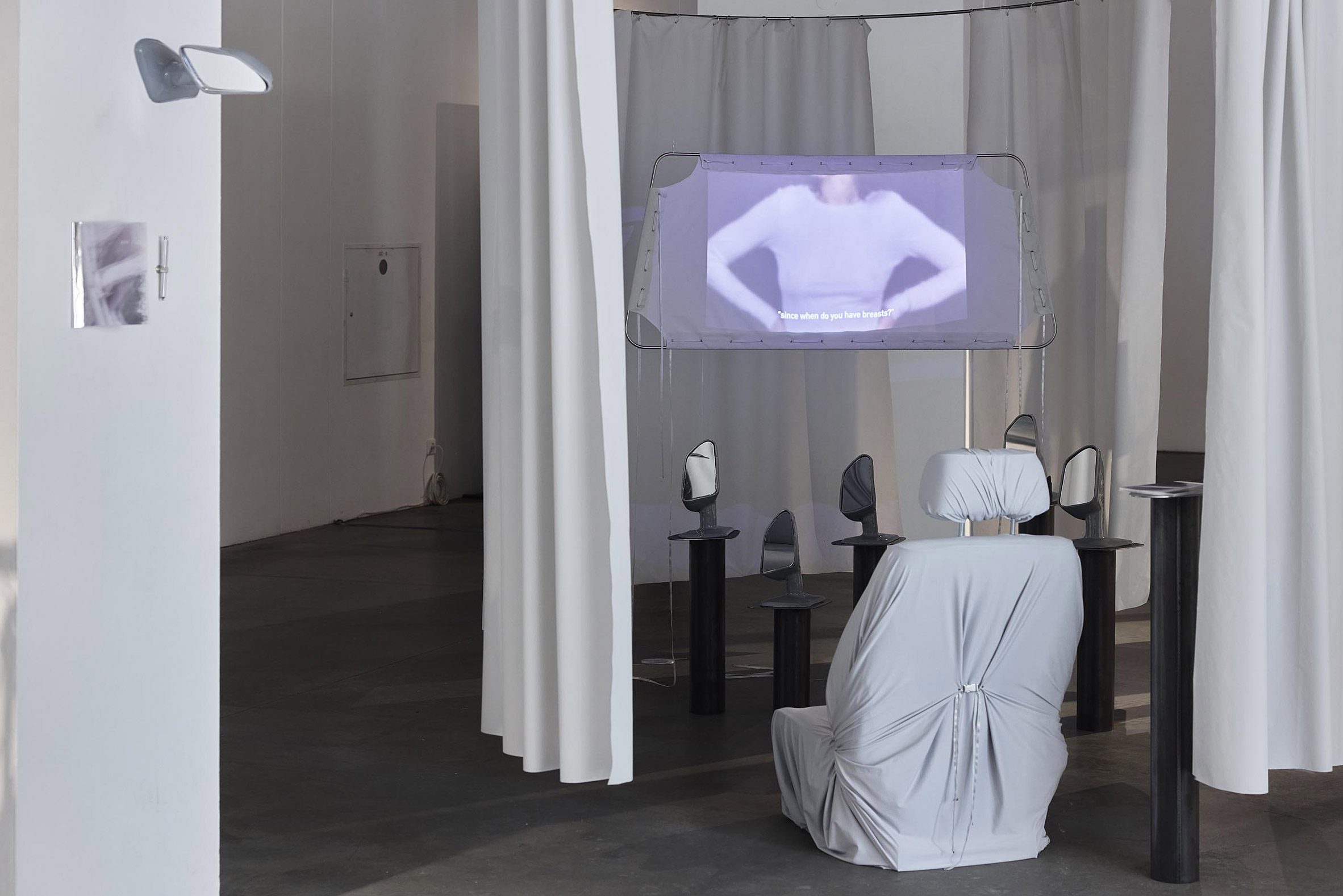 Photograph of an installation with a large, white chair facing a number of mirrors and a projector screen.
