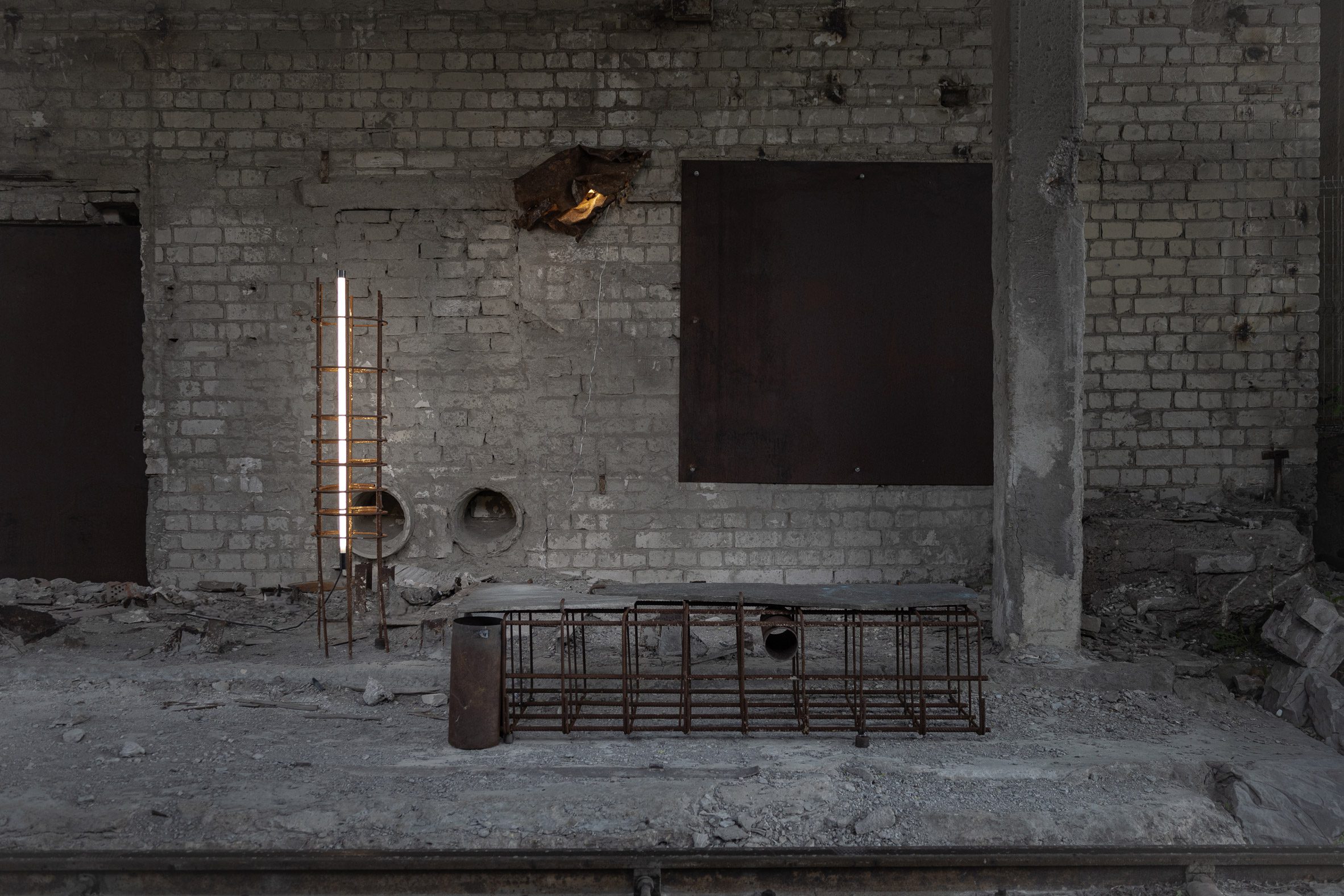 Image of a derelict basement-type space with concrete and a rusted metal bench.