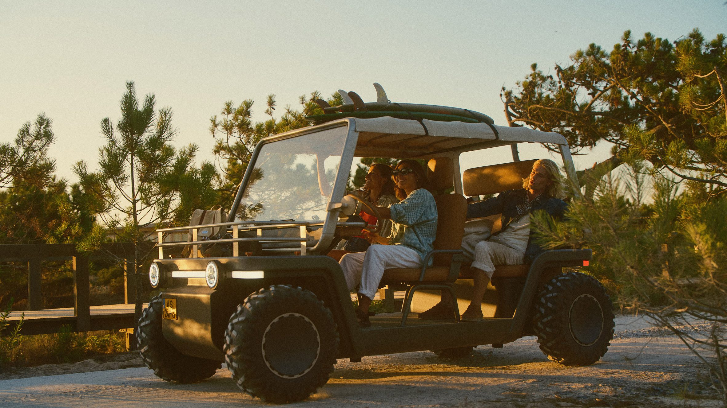 Foto do estilo de vida de um grupo de jovens dirigindo o buggy Amble One por um caminho costeiro com pranchas de surf amarradas no teto