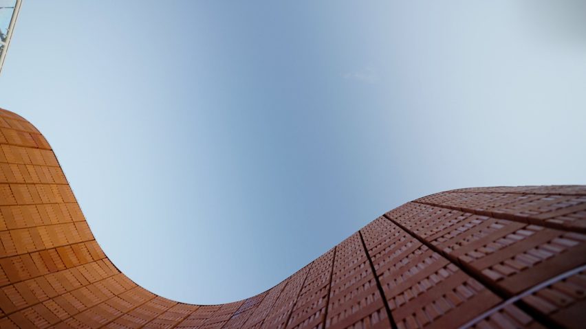 Low-angle view looking upward between two curving red-brick walls that frame a clear blue sky