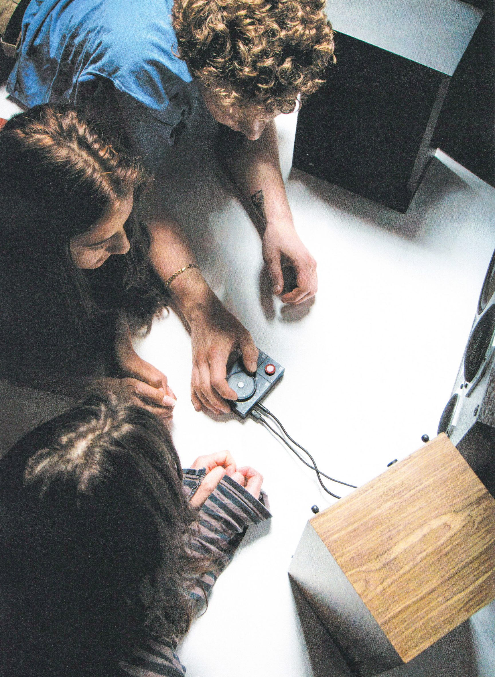Grainy photo of a group of young people crowded around the Atonemo NTS Radio Player device while one turns the wheel to select playlists