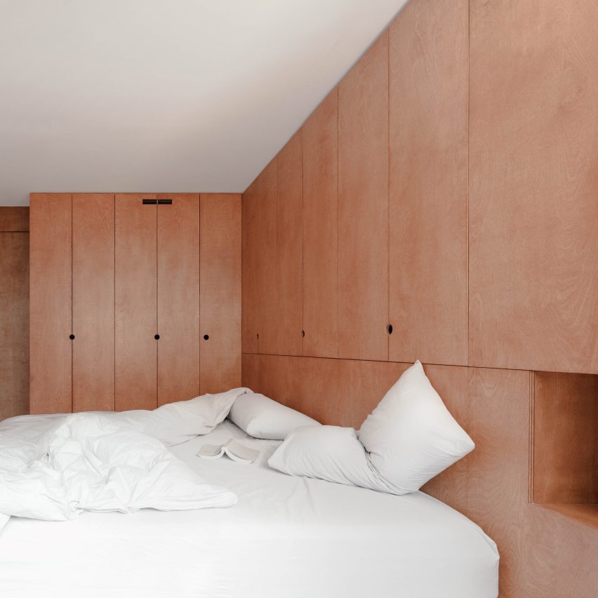 Bedroom with floor-to-ceiling plywood storage and an unmade bed