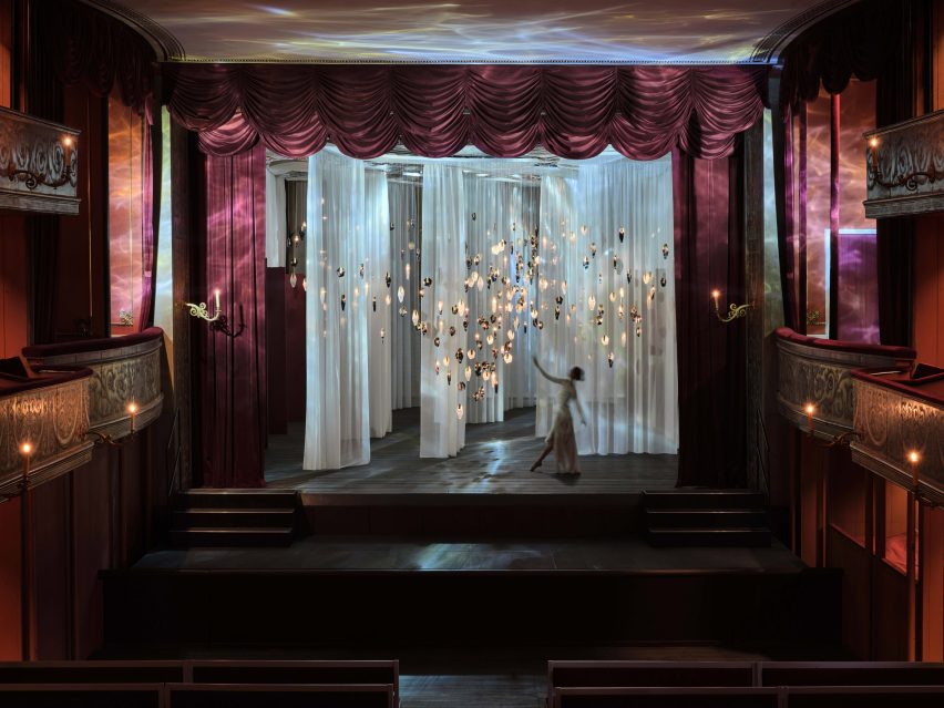 Crystal-like pendant lights suspended in front of translucent white curtains inside theatre